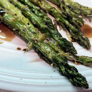 Roasted asparagus spears, seasoned and drizzled with a balsamic glaze and served on a white plate.