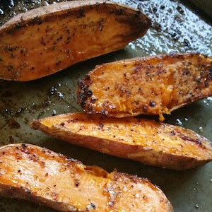 Roasted sweet potato halves with browned edges and seasoning served on a baking sheet.