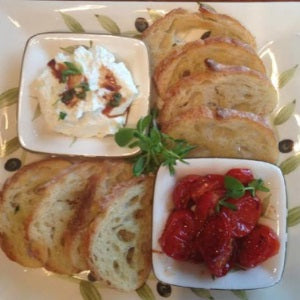 Toasted crostini served with whipped cheese topped with herbs and a side of roasted cherry tomatoes, arranged on a platter.