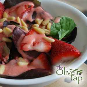 Leafy greens topped with sliced strawberries, pine nuts, and drizzled with a pink strawberry vinaigrette, served in a white bowl.