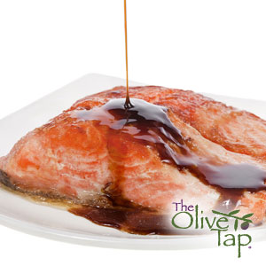 Baked salmon being drizzled with a balsamic glaze on a white plate with a white background.