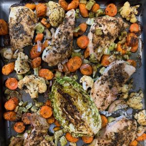 A pan of baked and seasoned chicken pieces, carrots, cauliflower, celery, and half of a cabbage.