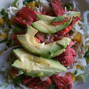 A bed of green cabbage topped with diced mango, green onions, smoked salmon, and avocado.