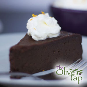A chocolate torte slice topped with whipped cream and orange zest, served on a white plate with a fork.