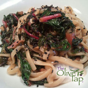 A pile of soba noodles with sauteed swiss chard with a sauce and sprinkled with black sesame seeds served on a white dish.