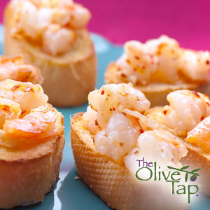 Slices of French bread topped with seasoned shrimp on a blue plate and pink background.