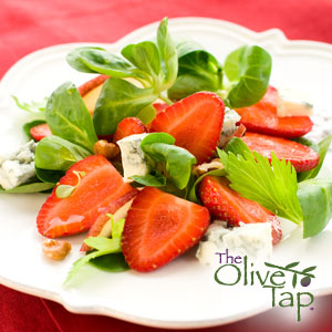 A bed of spring greens with halved strawberries, blue cheese, and chopped walnuts on a decorative white plate on a red tablecloth.