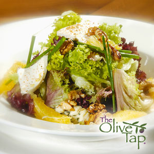 A bowl of spring mix with feta cheese, orange slices, chives, and walnuts in a white bowl on a wooden surface. 