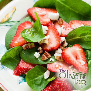 Spinach salad with fresh sliced strawberries, feta cheese, and chopped walnuts on a decorative plate.