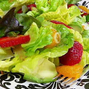 Spring salad mix topped with sliced strawberries, oranges, and avocado, served on a decorative plate.