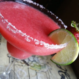 Frozen strawberry margarita with a salted rim and lime slice served in a margarita glass.