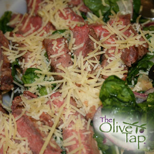 A salad of steak, artichoke hearts, and spinach topped with grated parmesan cheese.