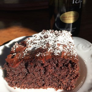A slice of dark chocolate balsamic cake dusted with powdered sugar and served on a white dessert plate.