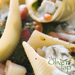 Large pasta shells stuffed with a creamy cheese filling, served in a rich sauce with vegetables and herbs, shown in a close-up view.