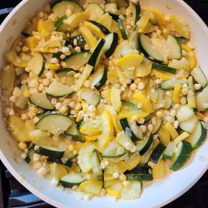 Salad of zucchini, summer squash, and corn in a white bowl.