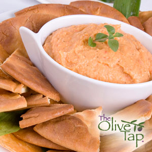 A bowl of hummus in a white bowl, garnished with a fresh green herb and surrounded by pita chips.