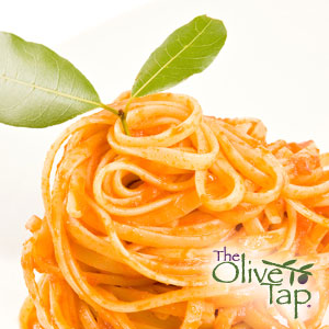 A close up of spaghetti noodles tossed in sun-dried tomato cream sauce garnished with a fresh green herb on a white background and The Olive Tap logo in the righthand corner.