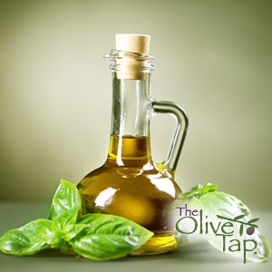 Glass bottle of olive oil surrounded by fresh basil leaves on a green background.