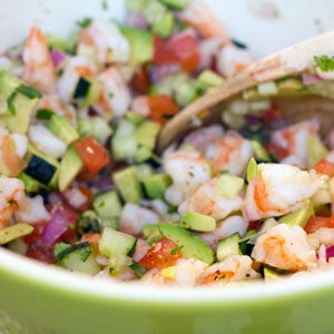 Close-up of ceviche made with chopped shrimp, avocado, red onion, tomato, cucumber, and cilantro, served in a green bowl.
