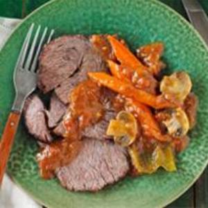 Sliced beef roast topped with carrots, onions, mushrooms, and savory sauce, served on a green plate.