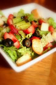 Romaine salad topped with croutons, black olives, and strawberry slices, drizzled with a vinaigrette and served in a white bowl.