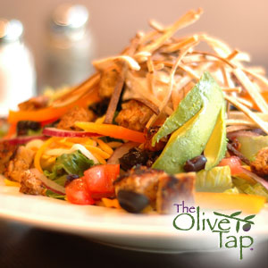 Colorful chopped salad topped with avocado slices, crispy tortilla strips, diced vegetables, and seasoned grilled chicken, served on a white plate.
