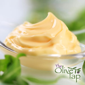 A glass bowl of cream-colored, whipped fresh mayonnaise surrounded by leafy greens.