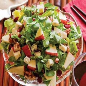 Leafy greens topped with apple pieces, walnuts, marshmallows, and dried cranberries, served in a glass dish.