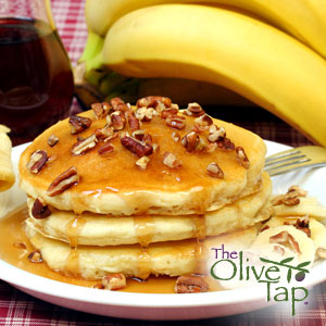 Stack of fluffy pancakes topped with chopped walnuts and maple syrup, served on a white plate with sliced bananas and whole bananas in the background.