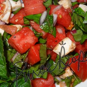 A salad of watermelon cubes, mozzarella cheese, chopped basil, and red onion, drizzled with a balsamic vinegar.
