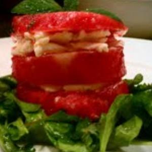 A round stack of watermelon slices, layered with goat cheese, on a bed of arugula and topped with fresh mint.