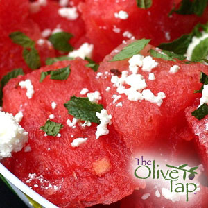 A close-up of watermelon cubes topped with chopped mint and feta cheese crumbles.