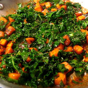 A pan of sauteed kale and diced sweet potatoes, drizzled with a vinaigrette.