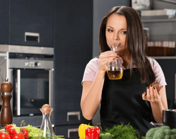 Woman smelling olive oil in the kitchen surrounded by vegetables.
