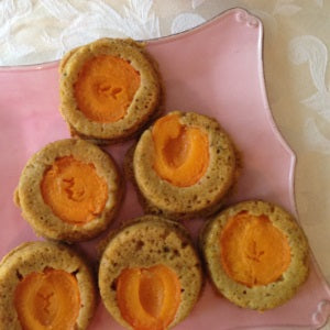 Little cakes with halved apricots in the center on a pink plate on a white tablecloth.