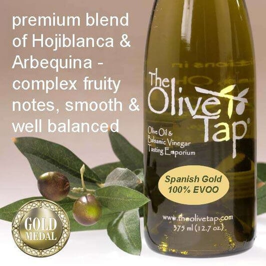 Bottle of Spanish Gold 100% Extra Virgin Olive Oil from The Olive Tap with olives and leaves including text describing the olive oil flavor profile on a light background.