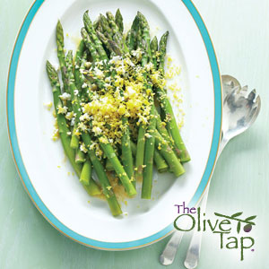 Roasted asparagus topped with parmesan cheese on a white and blue plate with utensils on a light blue surface.