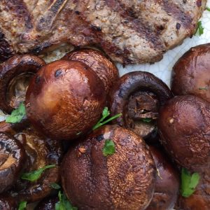 Whole mushrooms marinated in soy sauce on a plate with a grilled porkchop and garnished with chopped parsley.