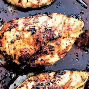 A close-up of baked chicken breasts in a black currant and blood orange sauce, sprinkled with herbs.