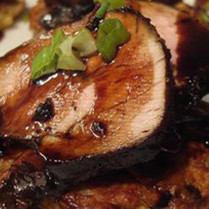 Sliced grilled pork tenderloin with a blackberry ginger sauce and garnished with green onion slices.