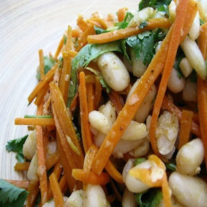 White beans, shredded carrots, and cilantro mixed together and served on a white plate.