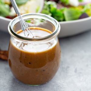 Creamy balsamic dressing in a glass jar with a salad in the background on a gray surface.