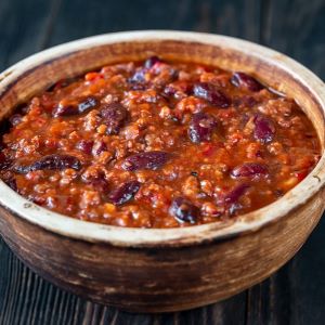 Hearty chipotle dark chocolate chili made with ground meat, kidney beans, tomatoes, and spices, served in a rustic wooden bowl and showcasing a rich, thick texture.