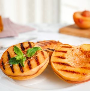 Halved grilled peaches garnished with mint on a white plate.