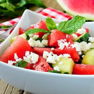 Watermelon and cucumber salad topped with fresh mint and feta cheese crumbles, served in a white bowl.