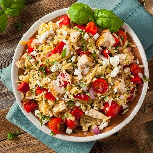 Bowl of orzo pasta salad with halved cherry tomatoes, diced chicken, cheese crumbles, and fresh basil.