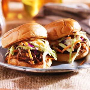 Two pulled pork sliders topped with colorful coleslaw and served on soft buns, arranged on a plate with a rustic table setting in the background.