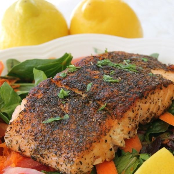 Seasoned salmon fillet served over a bed of mixed greens and sliced carrots, garnished with fresh herbs and accompanied by lemons in the background.