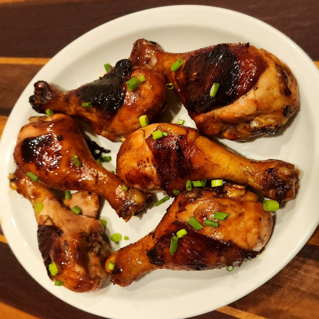 Bourbon maple glazed chicken legs with caramelized skin and chopped green onions served on a white plate.