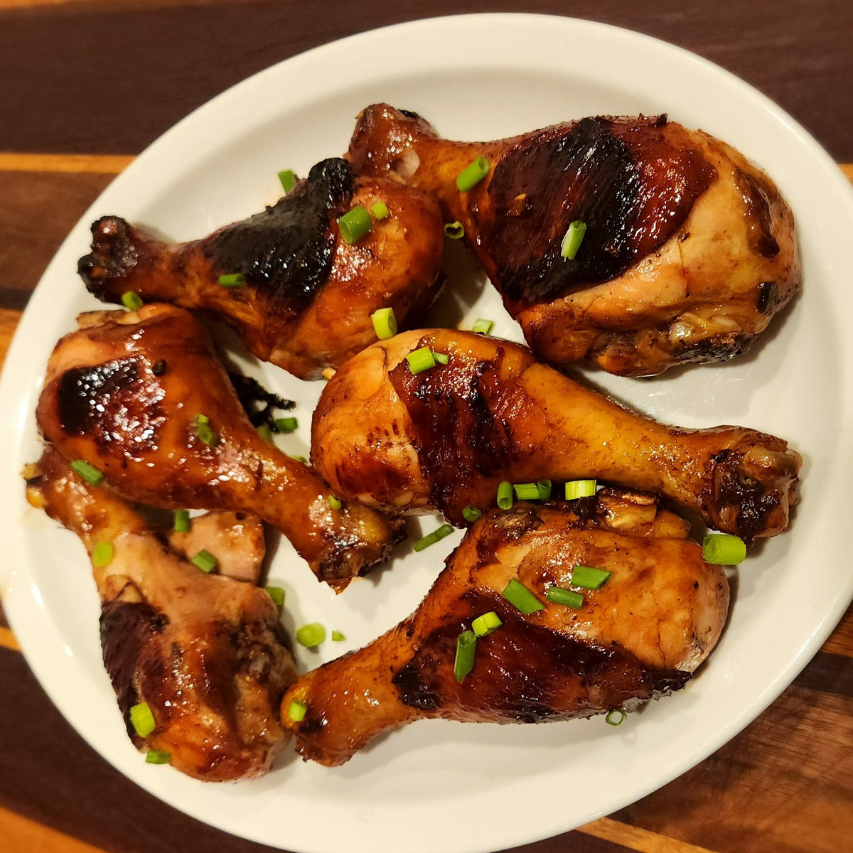 Bourbon maple glazed chicken legs with caramelized skin and chopped green onions served on a white plate.